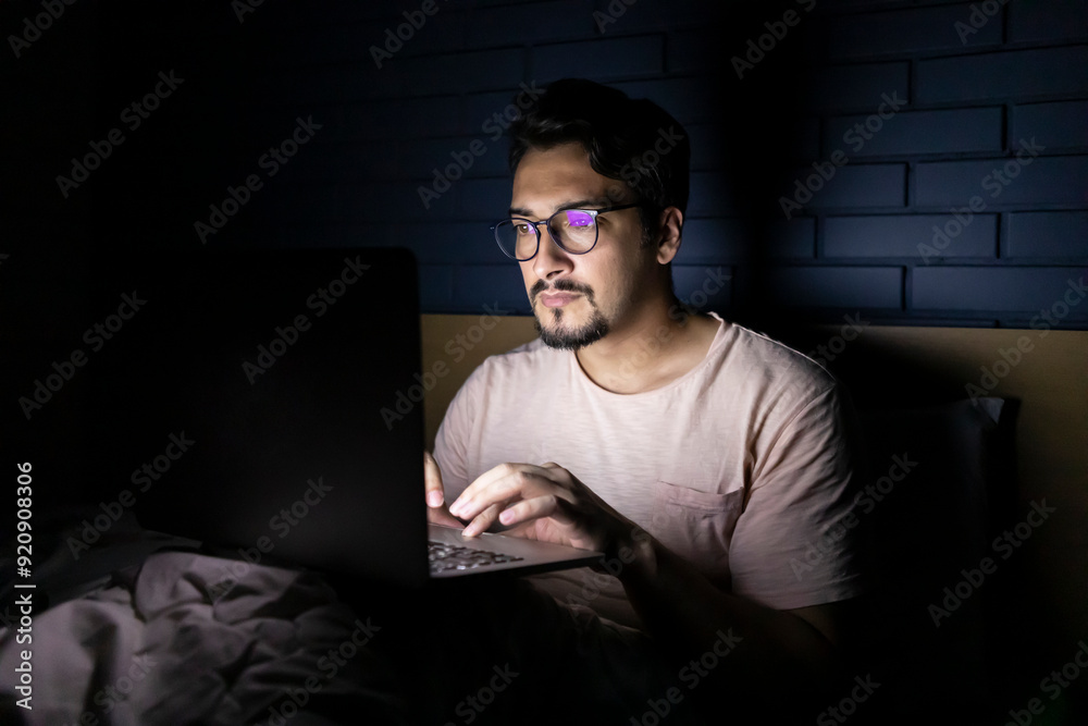 Concentrated man working on laptop in bed at night Concentrated man working on laptop in bed at night