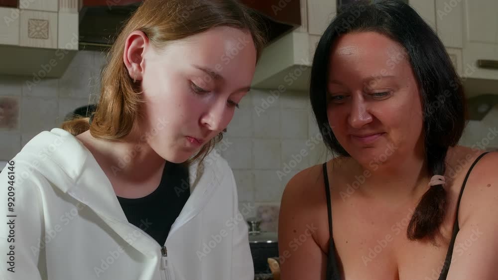 Smiling mother giving burger to daughter. Family is enjoying meal while eating together. They are in casuals while sitting in kitchen at home. Smiling mother giving burger to daughter. Family is enjoying meal while eating together. They are in casuals while sitting in kitchen at home.