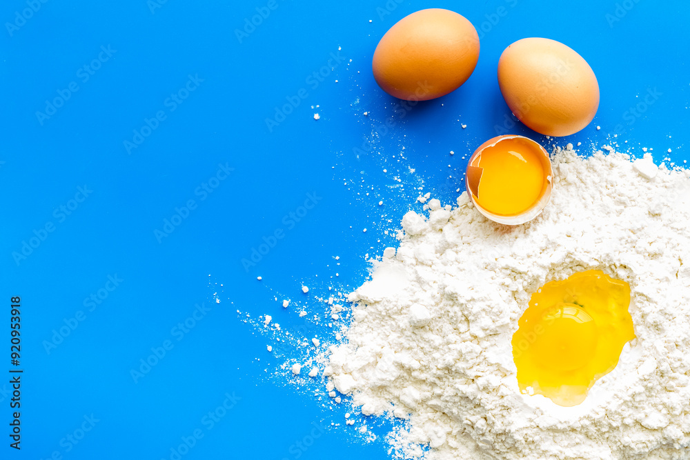Making dough concept. Pile of flour and eggs on blue background top view copy space Making dough concept. Pile of flour and eggs on blue background top view copy space