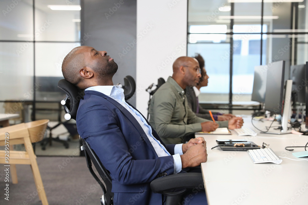 Businessman sitting with eyes closed at desk in office Businessman sitting with eyes closed at desk in office