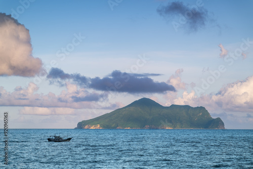 A serene coastal landscape featuring Turtle Island on the horizon. The island is framed by a vast expanse of blue ocean and a sky adorned with fluffy white clouds. Touchen, Yilan County, Taiwan. photo