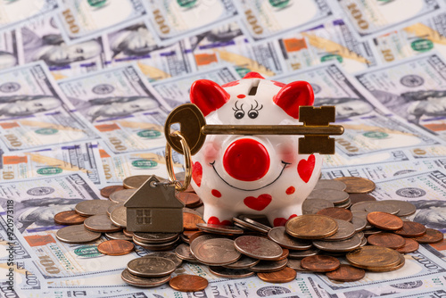 An apartment key with a keychain in the shape of a house, a funny piggy bank and American coins on a background of 100 US dollar bills photo