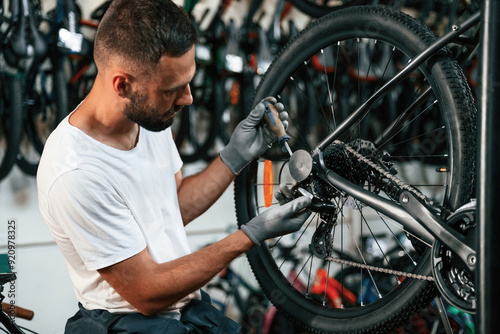 Spokes replacement. Repair man in bicycle shop, working in store