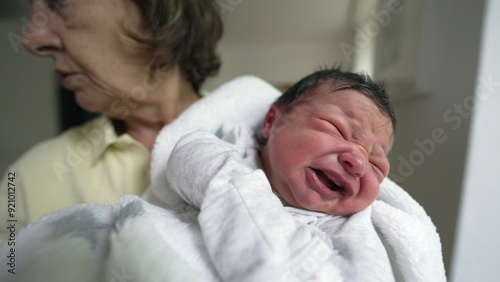 Concerned grandmother holding a fussy newborn baby wrapped in a white blanket. scene captures the love and care between them in a cozy home environment