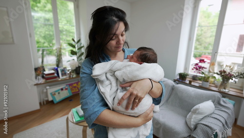 Mother cradling her newborn baby wrapped in a soft white blanket. The tender moment captures the love and bond between mother and child in a cozy home environment