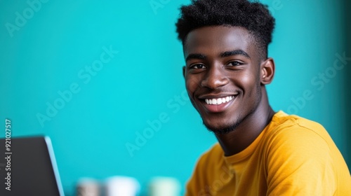 Smiling Young Man with Laptop on Teal Background photo