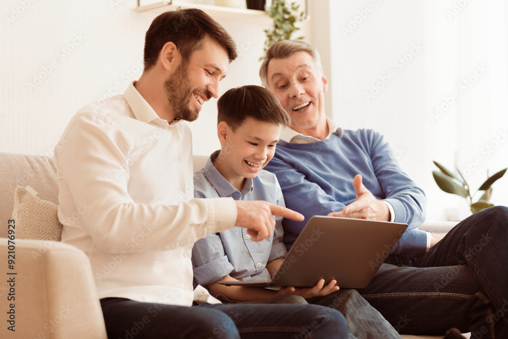 Happy Boy Using Laptop Sitting Between Father And Grandfather, Laughing And Having Fun Together On Couch At Home. Selective Focus Happy Boy Using Laptop Sitting Between Father And Grandfather, Laughing And Having Fun Together On Couch At Home. Selective Focus