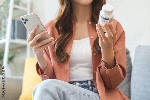 Health care asian young woman using smart phone for reading, searching prescription on bottle medicine, pill label text about information online, instructions side effects, pharmacy medicament concept