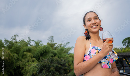 joven hispano latina tomando una copa de vino al aire libre y sonriendo felizmente photo