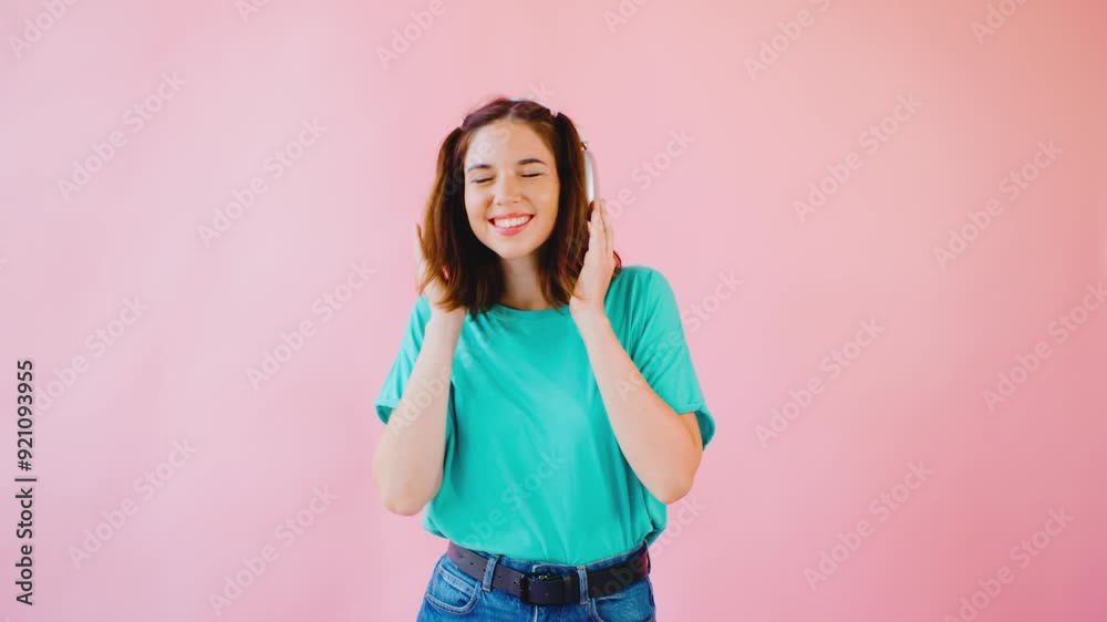 A joyful young woman is truly enjoying her music while wearing bright, colorful headphones that beautifully contrast against a vibrant pink background, embodying happiness and freedom A joyful young woman is truly enjoying her music while wearing bright, colorful headphones that beautifully contrast against a vibrant pink background, embodying happiness and freedom