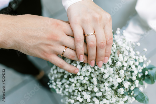 A pair of hands with wedding rings against a background of white flowers.