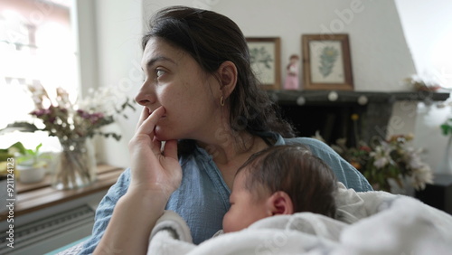 Fotografie Thoughtful mother holding newborn baby, gazing out of window, seated in a comfor