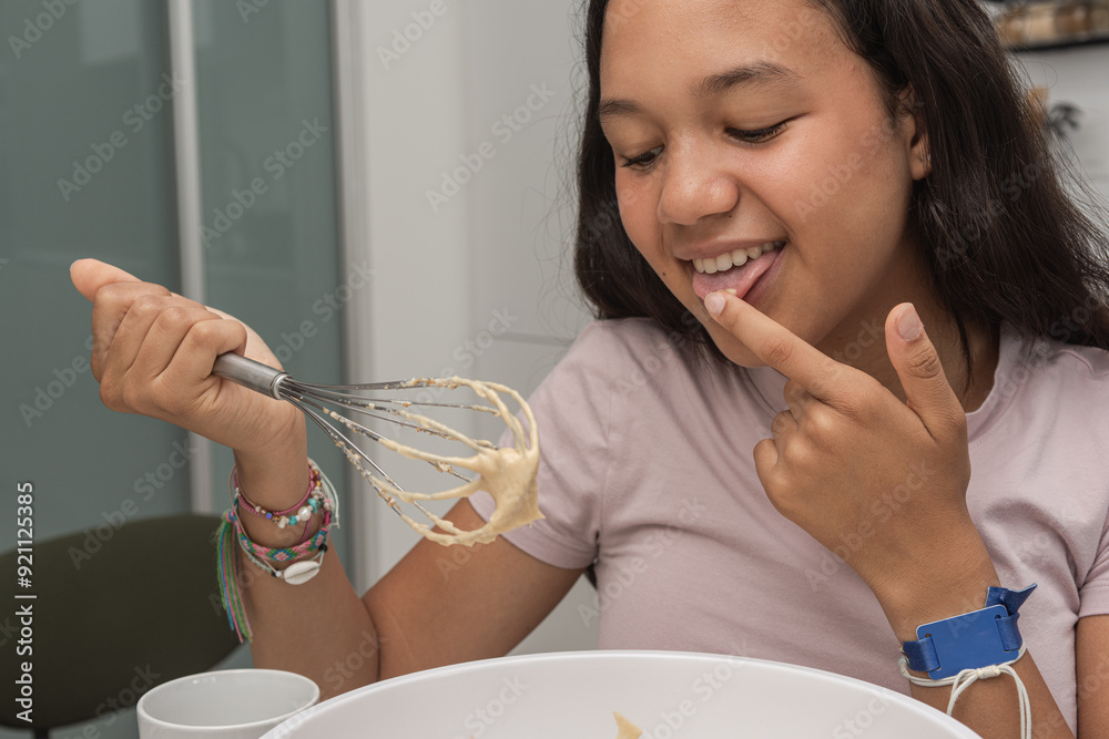 A teenager girl tasting the homemade cookie dough from the whisk. A teenager girl tasting the homemade cookie dough from the whisk.
