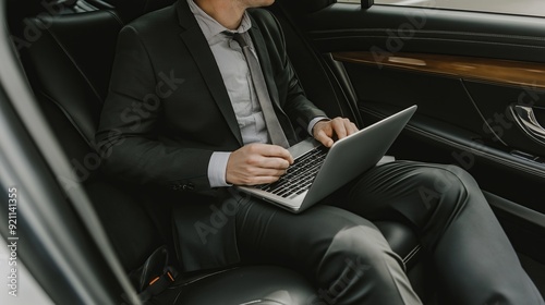 A professional man in a suit works on a laptop in a luxury car, exuding focus and determination.