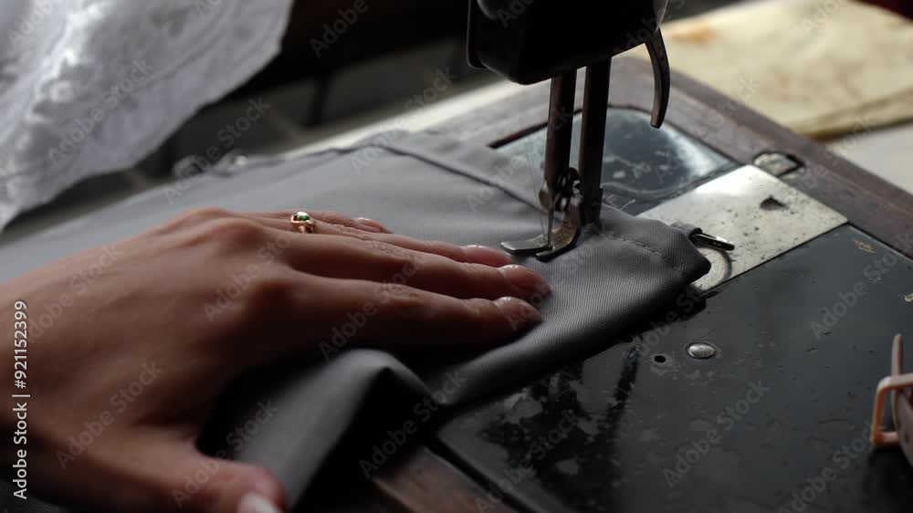 Hands deftly operate the mechanisms of a vintage sewing machine, showcasing the skilled craft of garment making and the timeless appeal of handmade textiles.