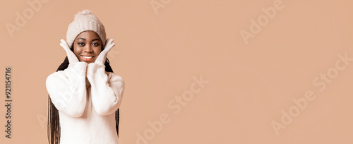 Fotografie A young black woman expresses joy by smiling broadly while wearing a cozy sweater and hat