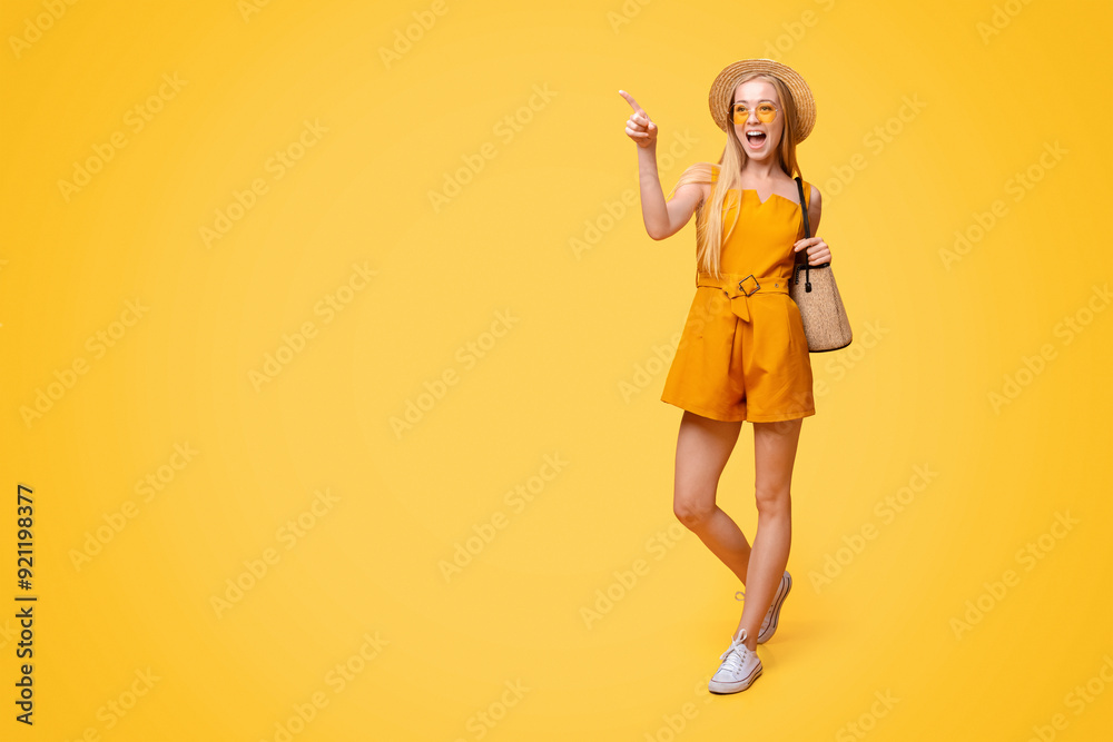 Summer Fashion. Stylish Young Girl Wearing Straw Hat And Sunglasses Walking With Bag And Pointing At Copy Space On Yellow Background