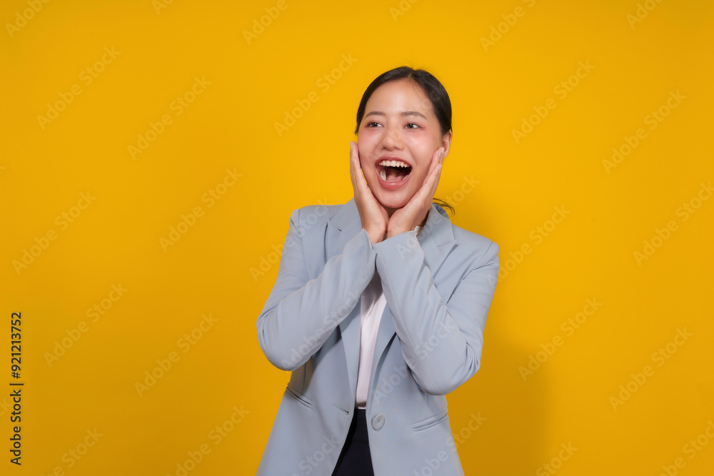 Asian businesswoman is posing on a yellow background, with an excited expression, holding her head in her hands Asian businesswoman is posing on a yellow background, with an excited expression, holding her head in her hands