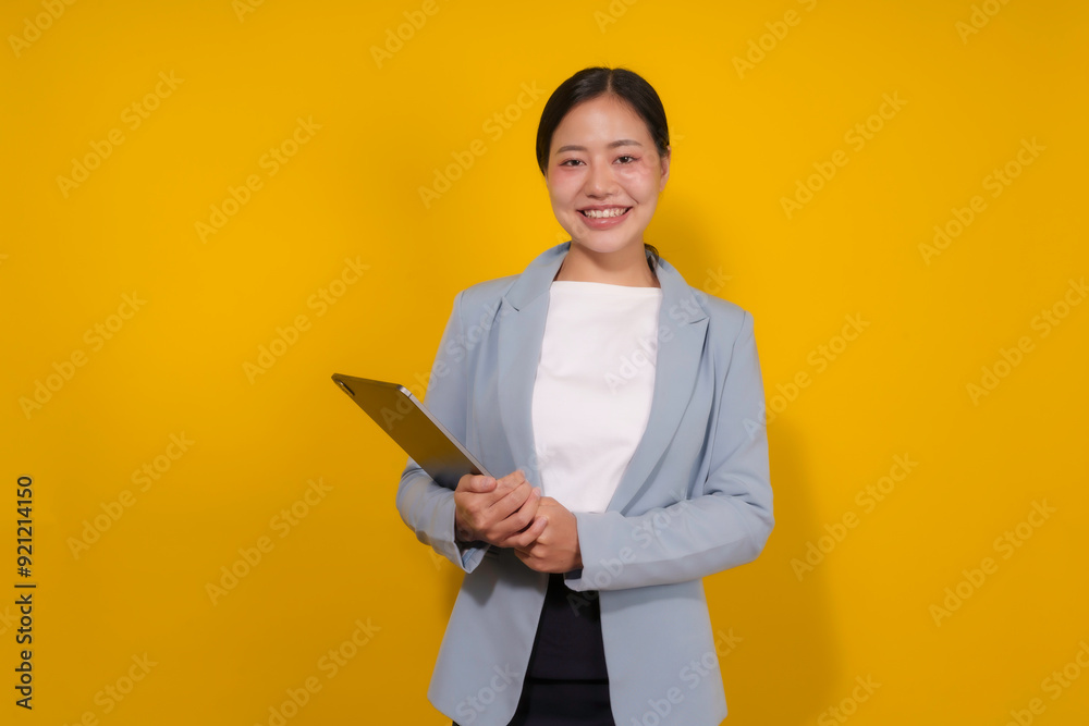Asian businesswoman is smiling while holding a digital tablet in her hands on a yellow background Asian businesswoman is smiling while holding a digital tablet in her hands on a yellow background