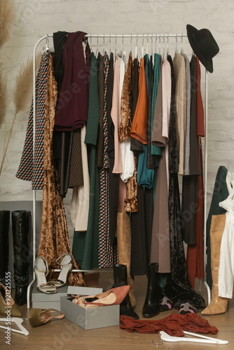 Untidy cluttered woman wardrobe with stylish clothes and accessories. Messy clothes thrown on a clothes rack, on the ground. Concept of over consumerism, shopaholic and compulsive buying disorder. photo