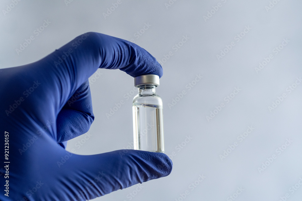 Naklejka premium A hand wearing a blue nitrile glove holding a small clear glass vial with a metal cap. The background is clear and uniform