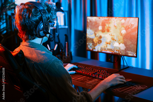 Host channel of young gaming streamer playing fighting Moba at battle arena game with multiplays team, wearing headphone on pc monitor with back side image at neon digital light modern room. Gusher. photo