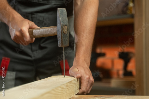 A person skillfully positions a nail against a piece of wood, preparing for a precise hammering technique. The focus is on the careful alignment needed for effective and accurate nailing as they bring