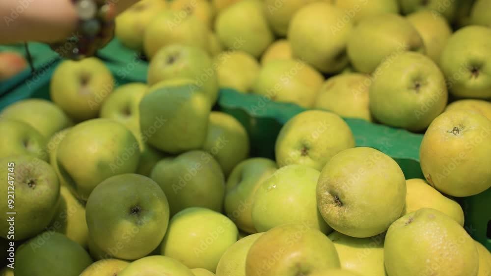 view of a hand wearing bead bracelets picking up two apples from a crate in a grocery store. Shot with a handheld camera view of a hand wearing bead bracelets picking up two apples from a crate in a grocery store. Shot with a handheld camera