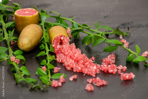 Ripe burgundy oblong fruits and delicious pink citrus caviar on the black slate slab decorated with a green plants sprig. Microcitrus australasica, Australian finger lime, Faustrimedin photo