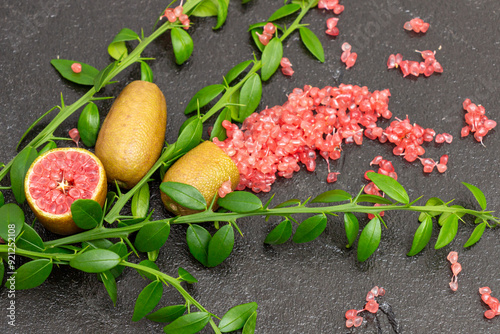 Ripe burgundy oblong fruits and delicious pink citrus caviar on the black slate slab decorated with a green plants sprig, close-up. Microcitrus australasica, Australian finger lime, Faustrimedin photo