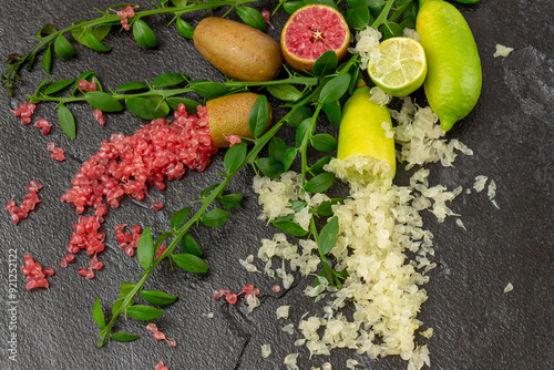 Ripe yellow and burgundy oblong citrus fruits with green sprigs on the black slate slab, close-up. Australian finger lime plant indoor growing. Microcitrus australasica, Faustrimedin