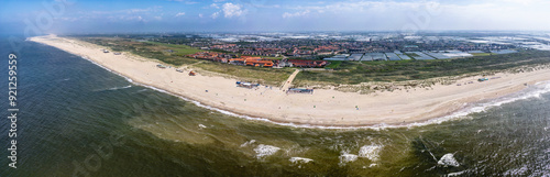 A panoramic view of Ter Heijde village shows an expansive sandy beach curving around a body of water, with buildings and farmland visible in the background. 