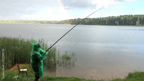 A man fisherman in a raincoat fishing in the lake. in inclement weather.