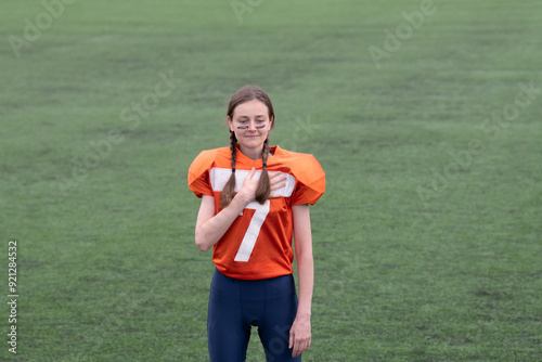 A girl or young woman with braids in an American football uniform holds her hand over her heart while playing the national anthem on a green grass background. photo