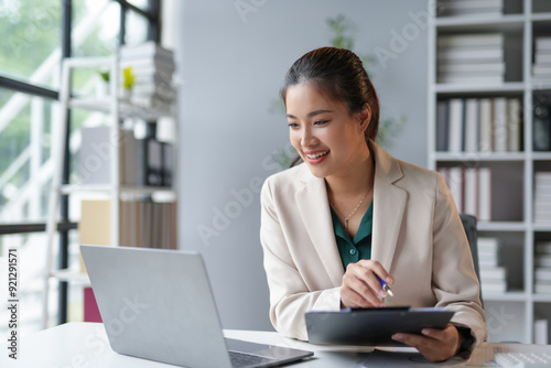 Young businesswoman is smiling while taking notes from the information she is reading on her laptop