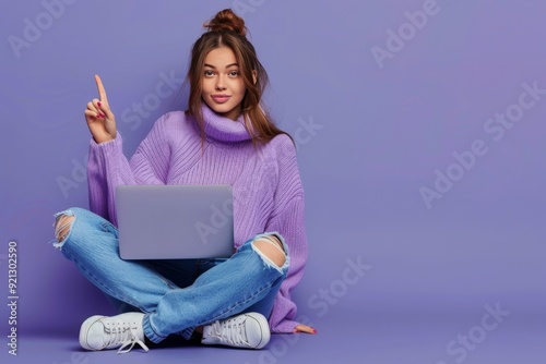 Full body photo girl sit floor legs crossed work laptop point index finger copyspace direct way follow comment ads wear lilac violet pullover denim jeans isolated blue color background