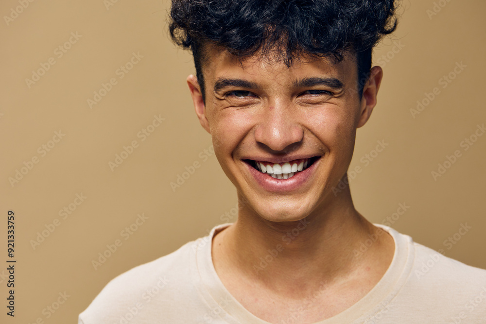 Happy young man smiling against a beige background, showcasing joy and positivity with natural lighting, capturing a moment of genuine happiness and warmth in a simple setting Happy young man smiling against a beige background, showcasing joy and positivity with natural lighting, capturing a moment of genuine happiness and warmth in a simple setting