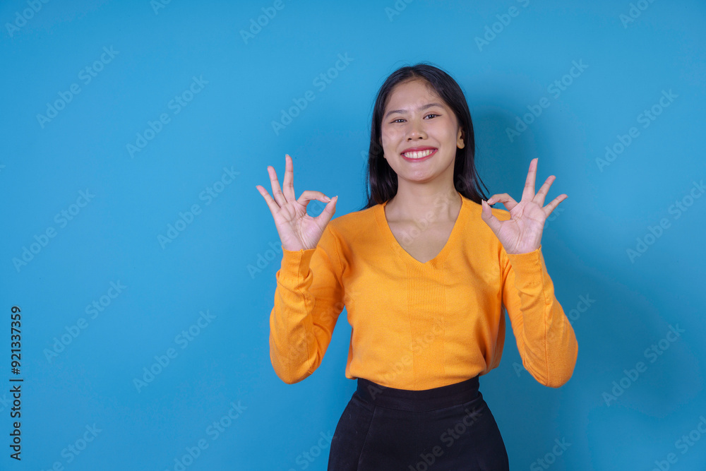 Young woman is posing on a blue background, smiling and showing the ok sign with both hands Young woman is posing on a blue background, smiling and showing the ok sign with both hands