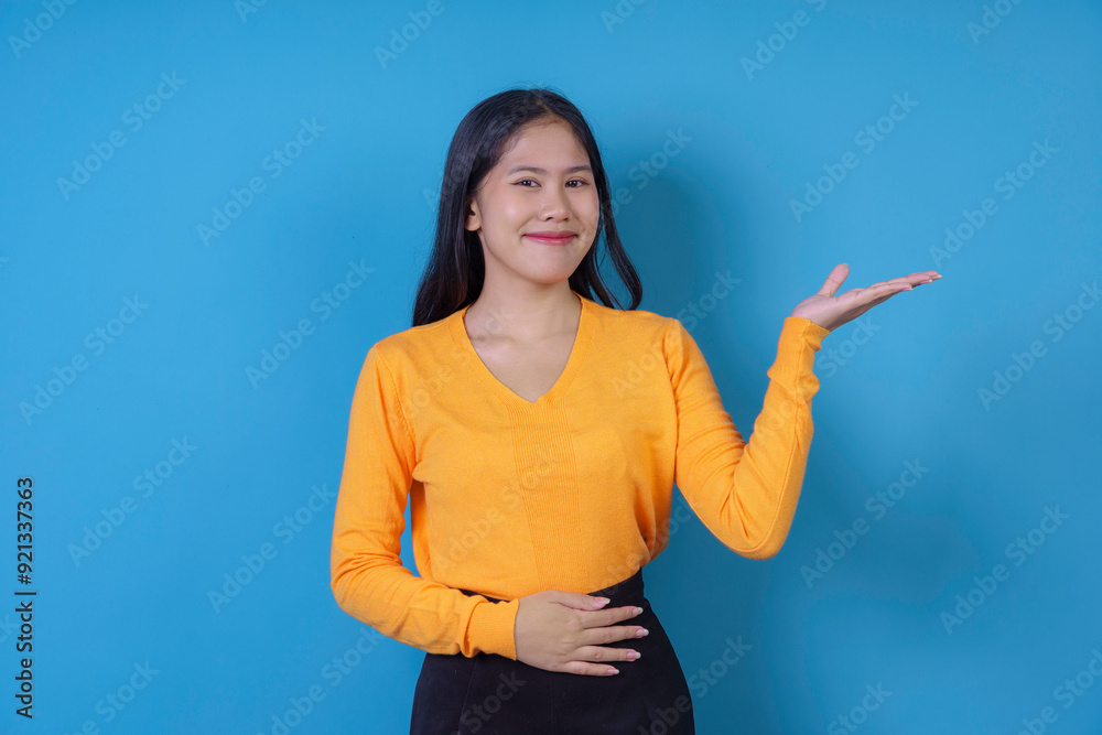 Young woman wearing a yellow sweater is posing with one hand on her stomach and the other one showing something on blue background Young woman wearing a yellow sweater is posing with one hand on her stomach and the other one showing something on blue background