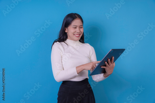 Young professional woman smiling and using a tablet against a blue background, expressing happiness and connectivity