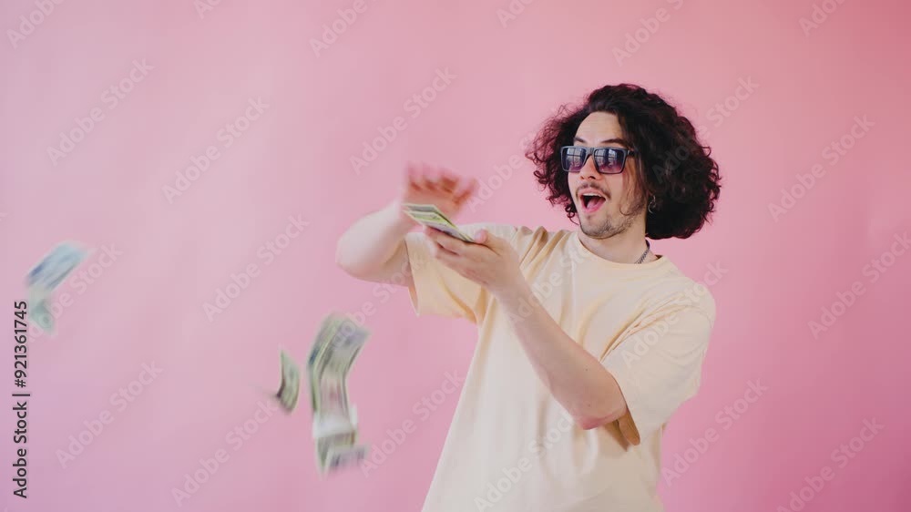 A curly-haired guy in a yellow shirt and sunglasses throws dollar bills in the air, standing in front of a bright pink background, giving off a confident and playful vibe. A curly-haired guy in a yellow shirt and sunglasses throws dollar bills in the air, standing in front of a bright pink background, giving off a confident and playful vibe.