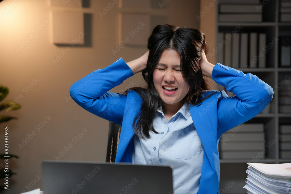 Young asian businesswoman is holding her head with her hands, stressed while working late at night in her office Young asian businesswoman is holding her head with her hands, stressed while working late at night in her office