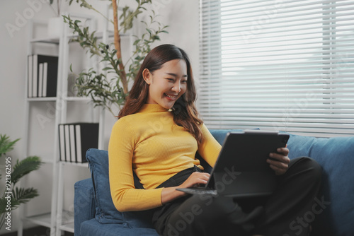Free Download Young asian woman is working from home, smiling while using her tablet computer on the sofa - GFXLoad