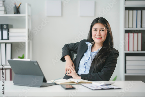 Young asian businesswoman smiling while sitting at her desk working on a laptop computer in a modern office