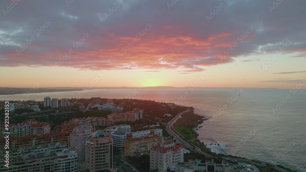 Fototapeta premium Vivid sundown shining ocean horizon over beautiful calm coastal town aerial view
