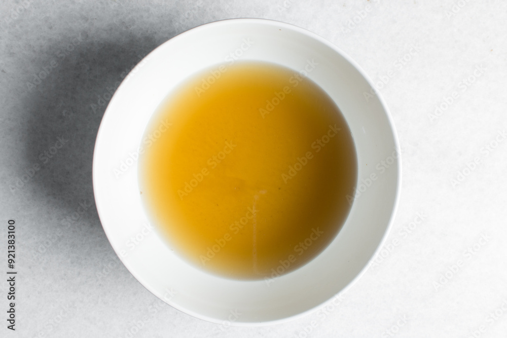 Overhead view of chicken broth in a white bowl, top view of cooked chicken beef broth, process of making broth Overhead view of chicken broth in a white bowl, top view of cooked chicken beef broth, process of making broth