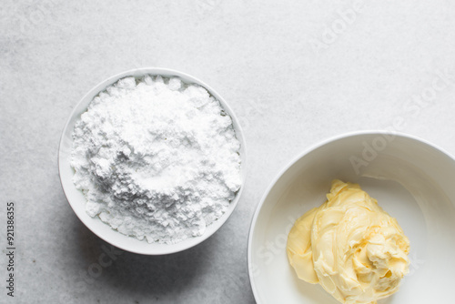 Overhead view of butter and icing sugar in a white mixing bowl, top view of margar and powdered sugar on a marble countertop, ingredients for making buttercream, process of making american buttercream