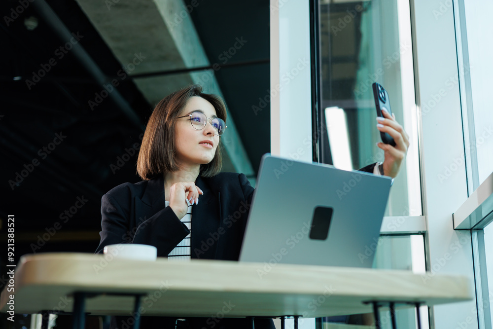 A young woman wearing glasses is sitting in a modern spacious working office. Woman office worker with laptop working. A young woman wearing glasses is sitting in a modern spacious working office. Woman office worker with laptop working.