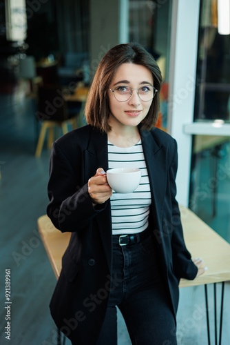 Free Download Concentrated business woman wearing glasses while working on a laptop computer while sitting in her spacious office with a cup of coffee on the table. - GFXLoad