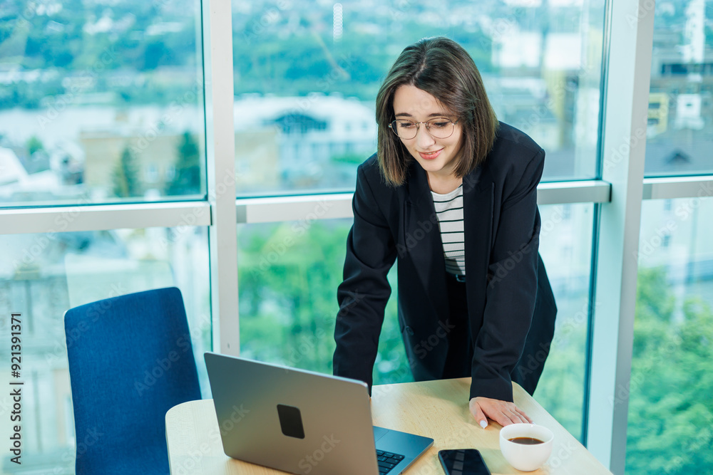 Businesswomen with coffee working on laptop in office, happy beautiful businesswomen in formal suit working at workplace. Emotions of a woman in the office. Businesswomen with coffee working on laptop in office, happy beautiful businesswomen in formal suit working at workplace. Emotions of a woman in the office.